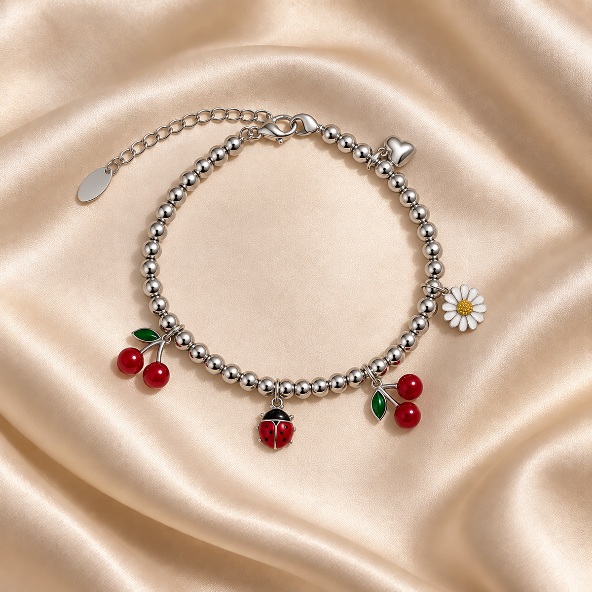 Silver Cherry & Ladybug Charm Bracelet on pale champagne satin, showing polished silver-tone beads, two cherry pairs, a red ladybug, white daisy, heart, clasp and extender.