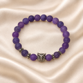 Purple Owl Bead Bracelet on pale champagne satin, showing matte purple crackle-pattern beads, a silver-tone owl centerpiece and decorative spacers.