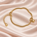 Golden Heart Knot Bracelet with double gold-tone chains, a small heart charm and extender, laid on champagne satin.