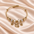 Moon & Star Bead Cuff Bracelet on pale champagne satin, showing its overlapping gold-tone wire, white beads, iridescent accents and moon-and-star charms.