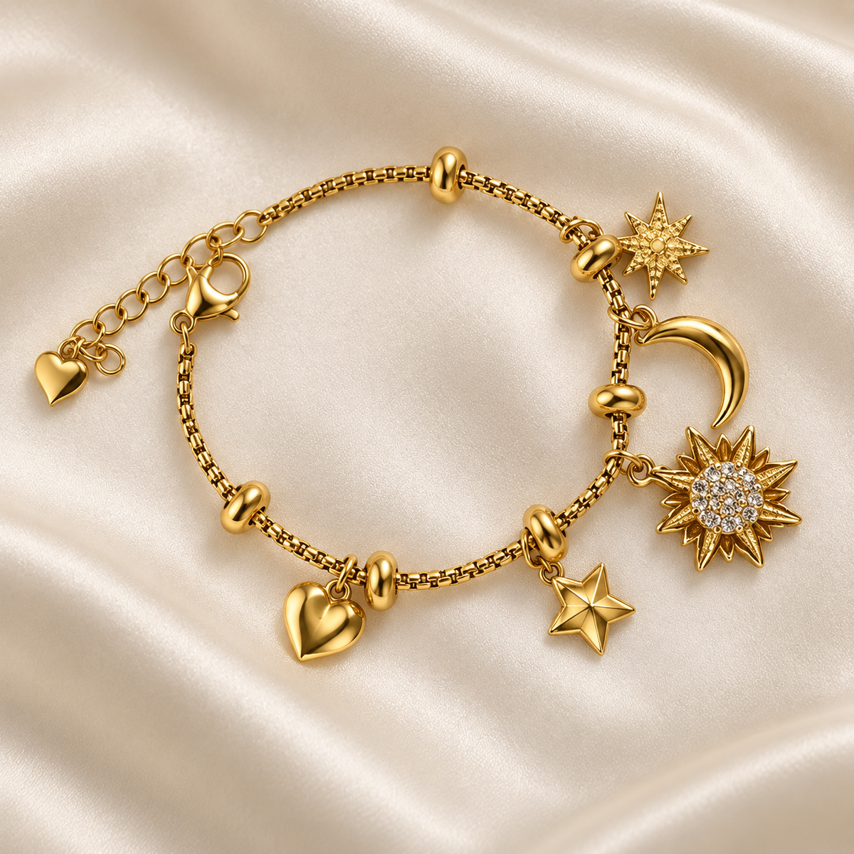 Gold-tone sun and moon charm bracelet with heart, star, sunburst, and crescent details on ivory satin