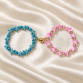 Starfish Friendship Bracelet Pair on pale champagne satin: turquoise-blue starfish bracelet and pink-and-white starfish bracelet connected by a gold-tone split heart.