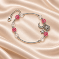 Pink Moon & Star Bracelet on pale champagne satin, with silver-tone curved bars, textured pink and clear beads, celestial charms and extender visible.