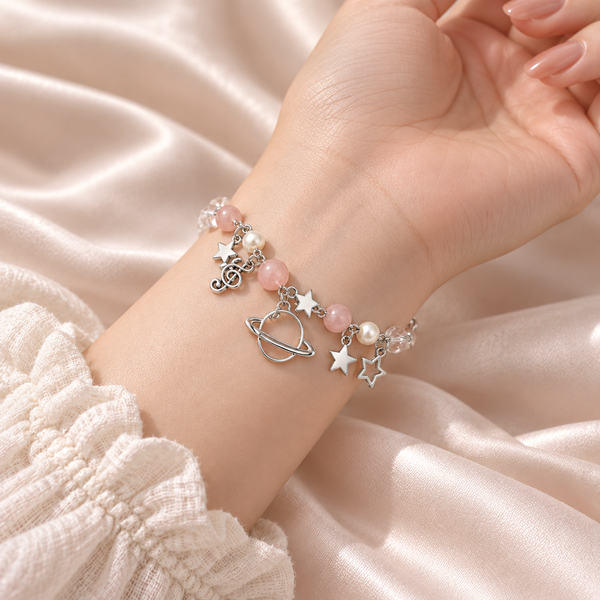 Snug close-up of the silver-tone Celestial Orbit Charm Bracelet around a wrist, with pale pink and pearl-like beads, ringed planet, star and music-note charms.