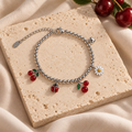 Silver Cherry & Ladybug Charm Bracelet styled on ivory stone and linen, with bright silver beads, cherry pairs, a red ladybug and white daisy.