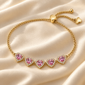 Five pink heart accents on the Blush Heart Slider Bracelet, arranged on cream satin with its gold-tone chain and heart-shaped slider visible.