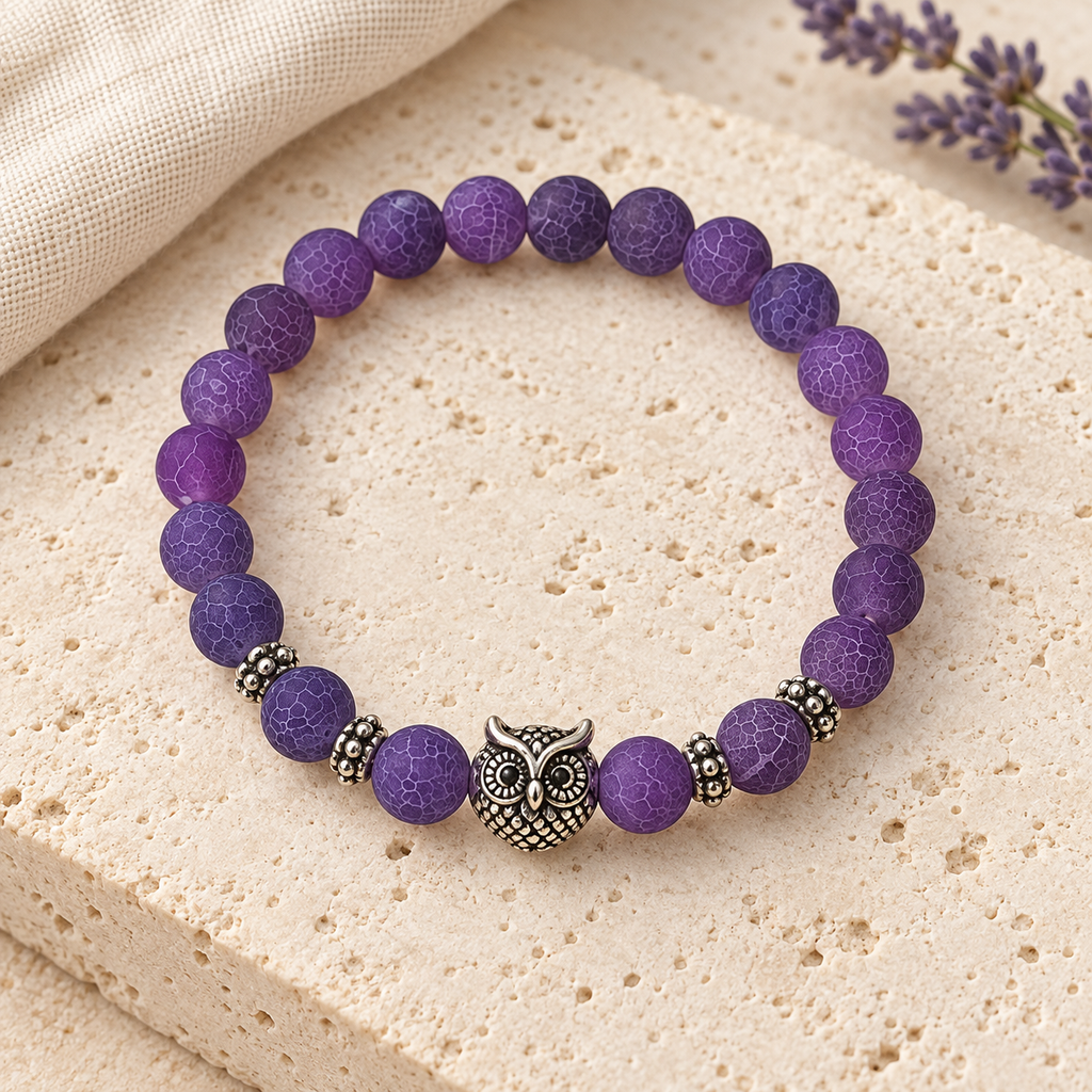 Purple Owl Bead Bracelet styled on ivory stone and linen, showing the purple beads, owl centerpiece and silver-tone spacers.