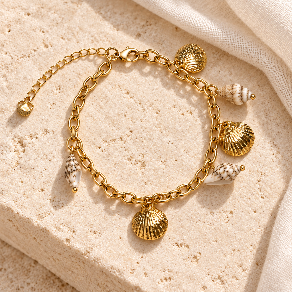 Seashell Treasures Charm Bracelet styled on ivory stone and linen, with three gold scallop charms and cream shell-look accents.