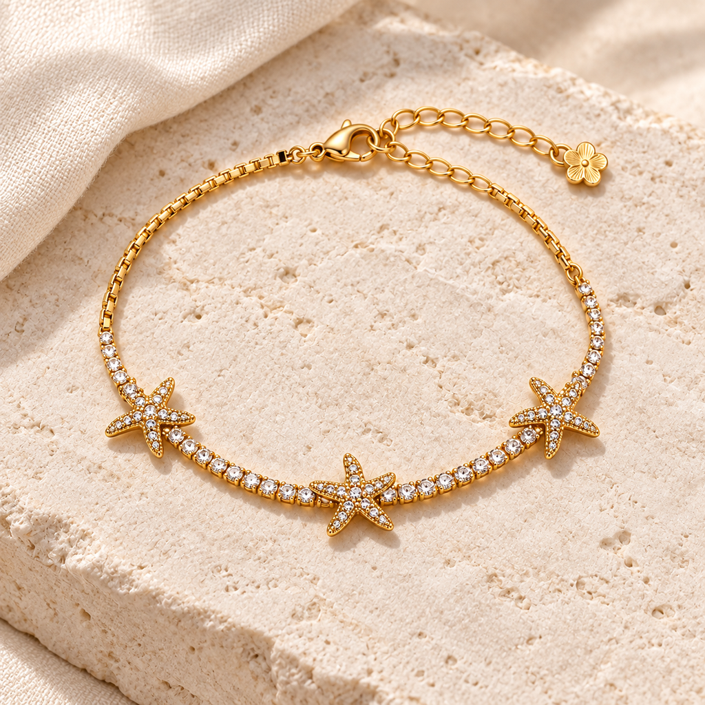 Starfish Sparkle Bracelet styled on ivory stone and linen, with three sparkling starfish across a gold-tone chain.