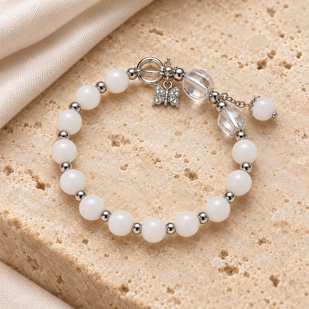 Snow White Bead Bracelet styled on ivory stone and linen, showing white beads, silver-tone spacers, clear accents and butterfly detail.