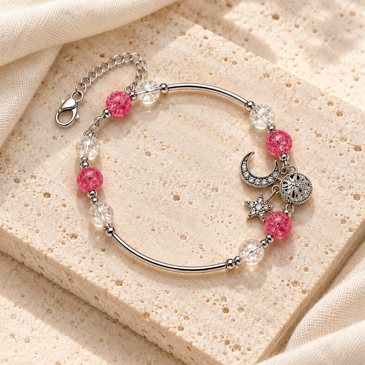 Pink Moon & Star Bracelet styled on ivory stone and linen, showing its silver-tone bars, pink textured beads, clear beads, charms, clasp and extender.