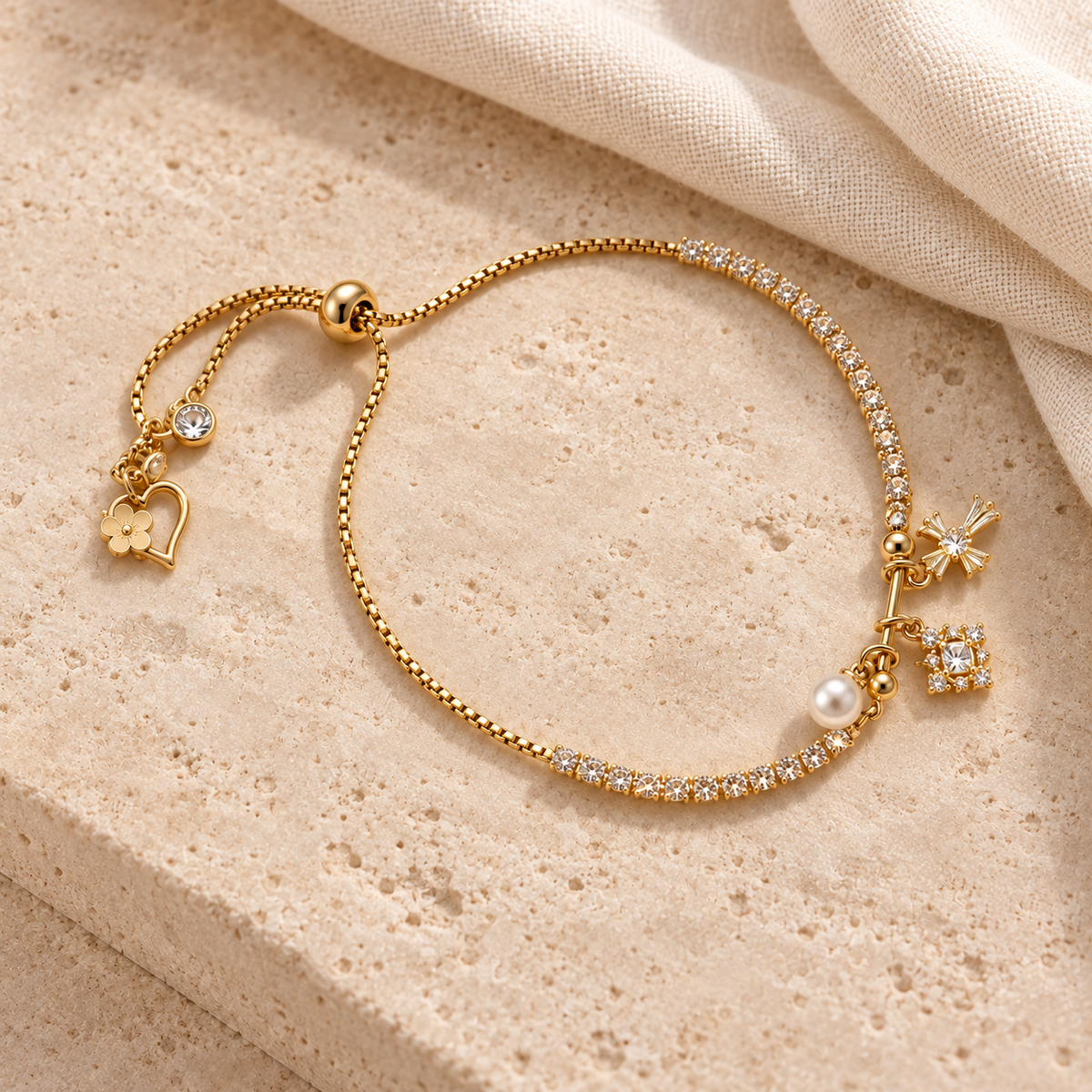 Golden Sparkle Charm Slider Bracelet styled on warm beige stone and cream linen, with clear sparkling details and a white pearl-style accent.