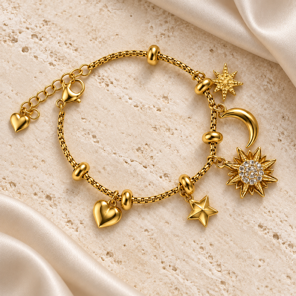 Gold-tone heart, star, sunburst, and crescent charm bracelet styled on pale travertine with ivory silk