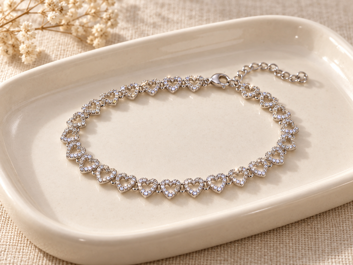 Silver-tone repeating heart bracelet arranged on an ivory ceramic tray