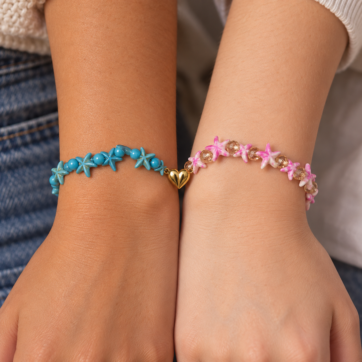 Two friends wearing matching Starfish Friendship Bracelets snugly around their wrists, one blue and one pink, with the gold-tone split heart meeting between them.