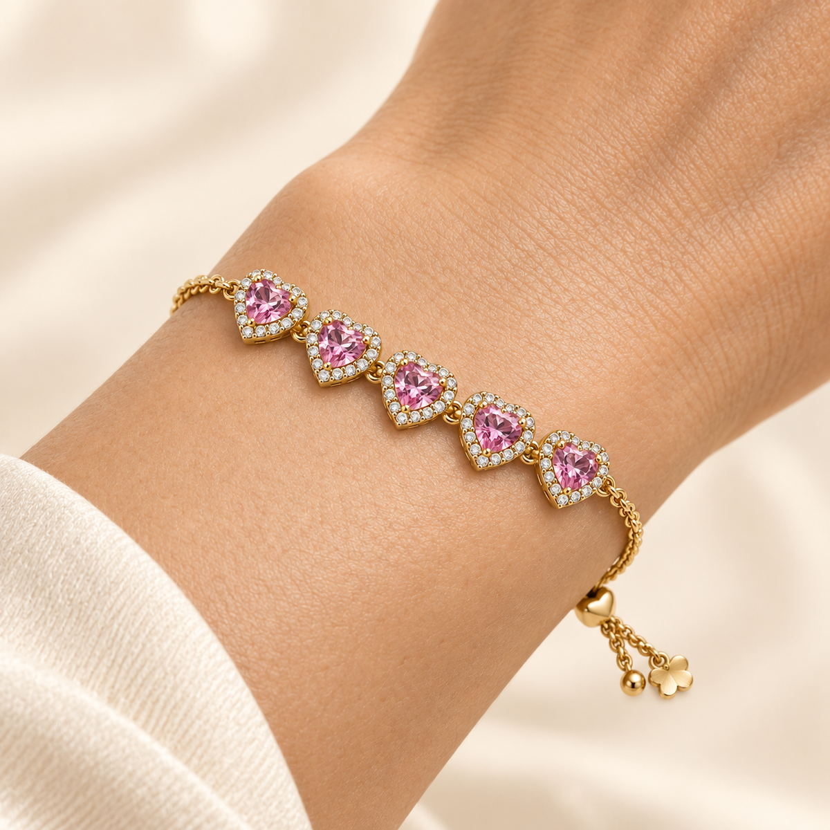 Close-up of five pink hearts on the Blush Heart Slider Bracelet worn snugly around a wrist, with the fine gold-tone chain and tightened heart slider visible.