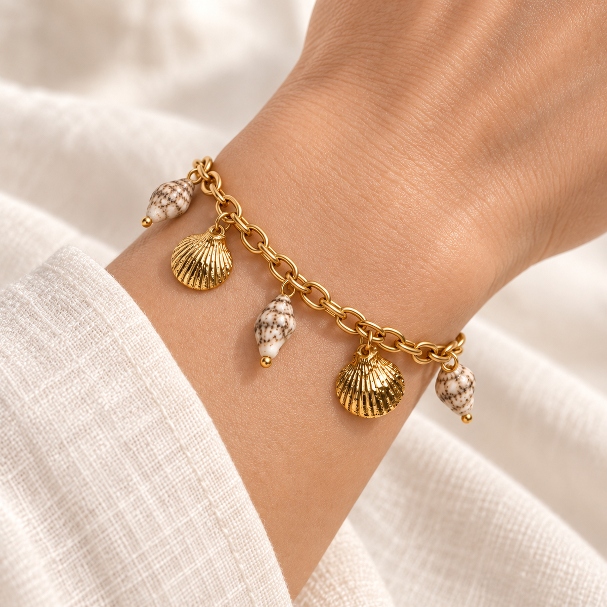 Close-up of the Seashell Treasures Charm Bracelet fastened snugly around a wrist, showing gold scallop and cream shell-look charms.