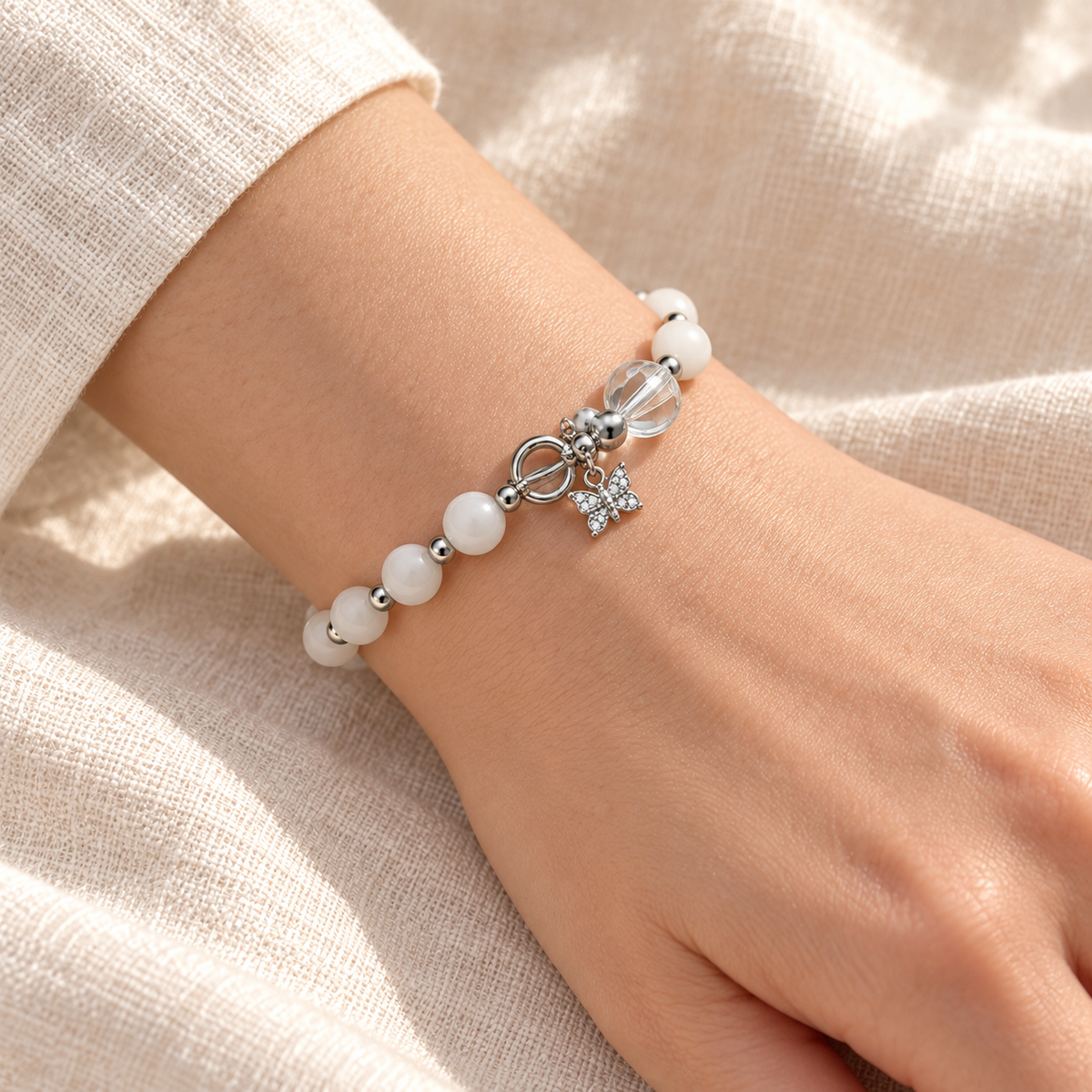 Close-up of the Snow White Bead Bracelet fastened snugly around a wrist, with white beads, silver-tone spacers and butterfly charm.