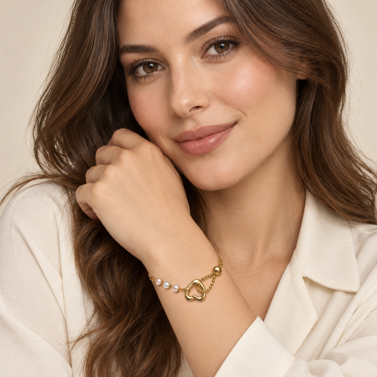 Portrait showing a model’s face and the Golden Heart & Pearl-Style Bracelet worn snugly around her wrist, with a gold-tone open heart, three pearl-like beads and asymmetric chains.
