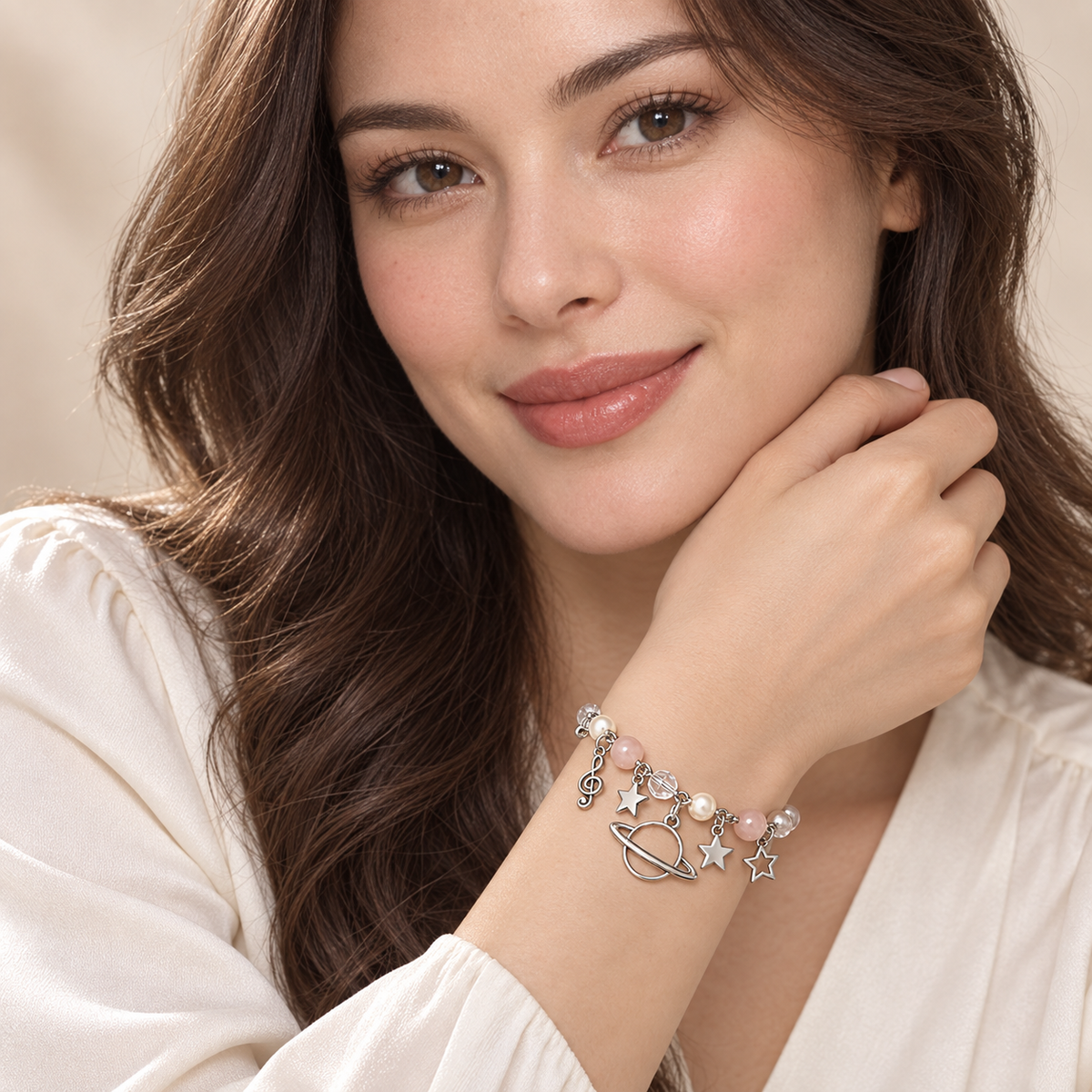 Portrait showing a model’s face and the silver-tone Celestial Orbit Charm Bracelet worn snugly on her wrist, with a ringed planet, stars, pale pink beads and pearl-like accents.