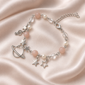 Celestial Orbit Charm Bracelet with silver-tone ringed planet and star charms, blush and pearl-like beads, on ivory satin.