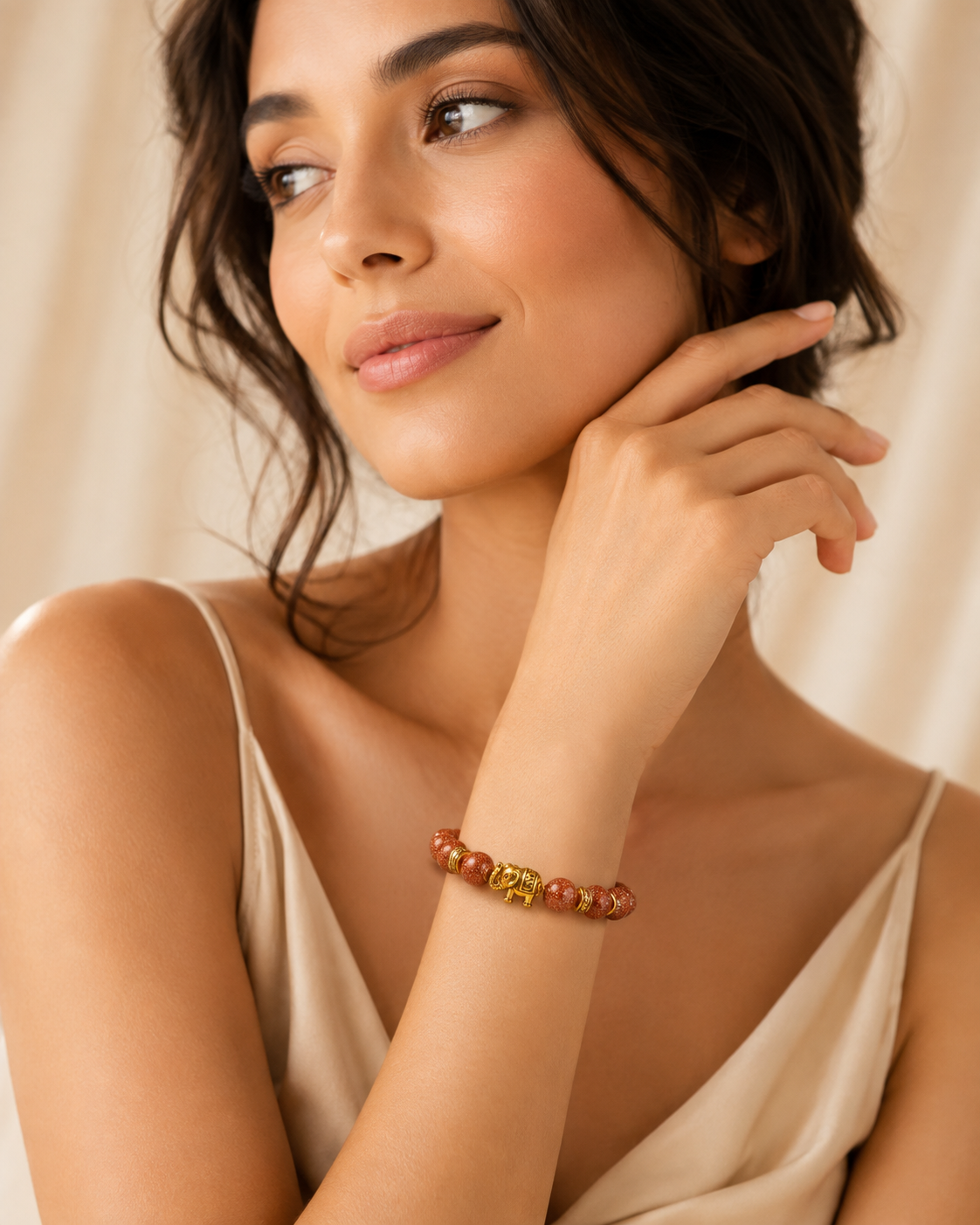 Model wearing the Elephant Charm Bracelet with warm brown sparkle beads, gold spacer accents, and a gold elephant charm styled with a cream outfit.