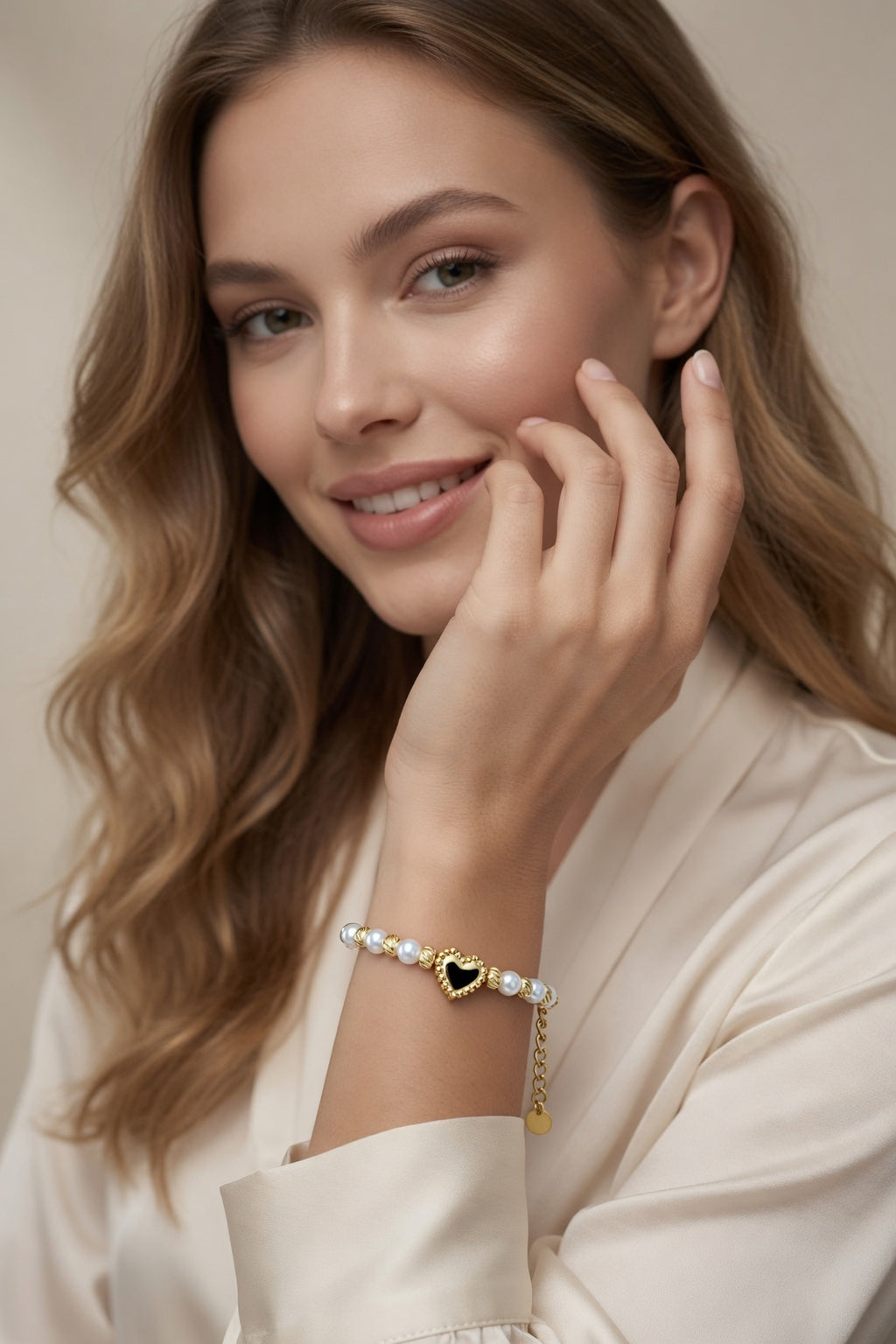 Model wearing the Golden Pearl Heart Bracelet with white pearl beads, gold swirl spacers, heart centerpiece, and adjustable chain styled with a cream outfit.