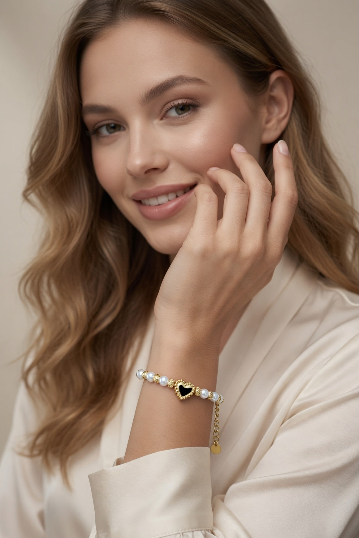 Model wearing the Golden Pearl Heart Bracelet with white pearl beads, gold swirl spacers, heart centerpiece, and adjustable chain styled with a cream outfit.