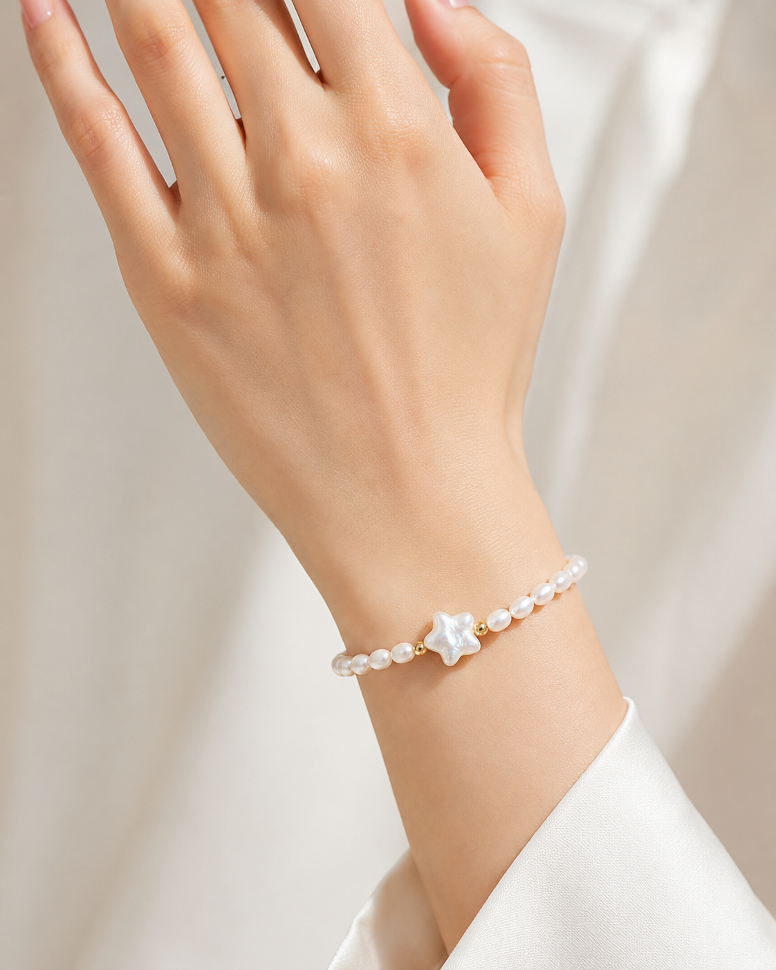 Close-up of a hand wearing a delicate pearl bracelet with a white star-shaped accent and small gold beads.
