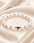 Blush Heart Bracelet with faceted blush-white beads, gold spacer beads, and gold heart centerpiece on satin fabric.