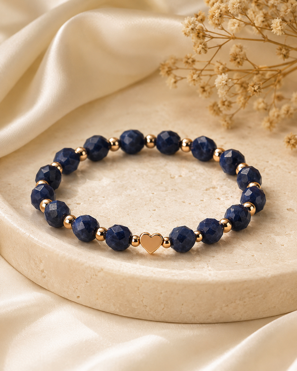 Navy-blue and gold heart bracelet displayed on a neutral marble tray with soft luxury styling.

