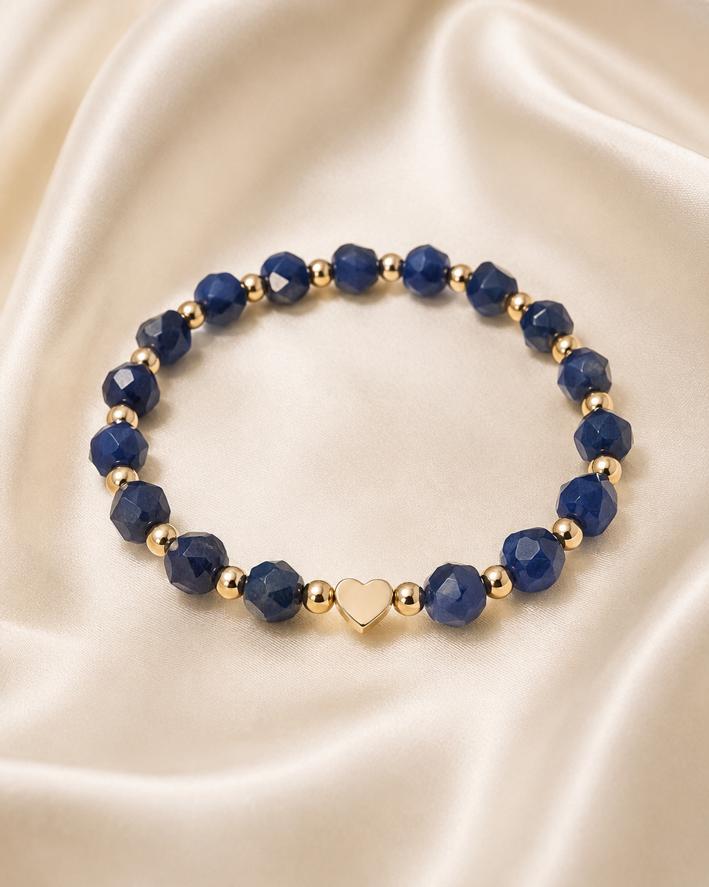 Midnight Heart Bracelet with navy-blue faceted beads, gold spacer beads, and gold heart centerpiece on satin fabric.
