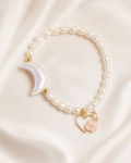 Moonlit Pearl Bracelet with freshwater pearls, iridescent crescent moon, gold spacer beads, and Ohana charm on ivory fabric.