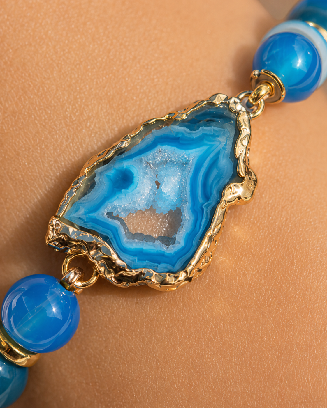 Close-up of blue agate centerpiece with layered blue bands, crystal detail, gold edging, and blue beads.
