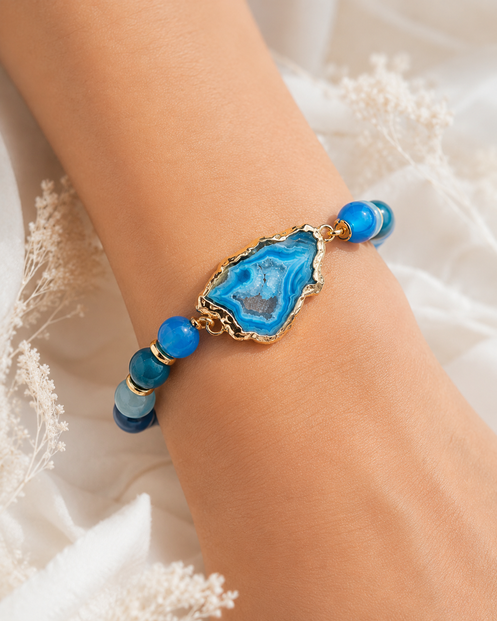 Ocean-inspired blue beaded agate bracelet with gold accents styled on wrist with white sleeve.