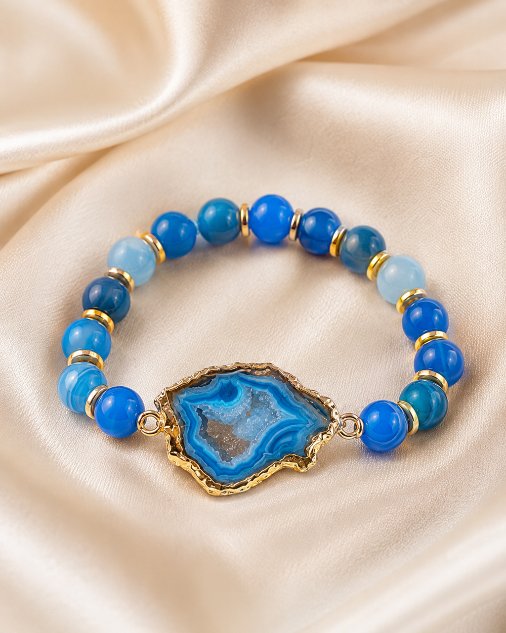 Blue agate bracelet with glossy blue beads and gold spacer accents displayed on ivory satin.