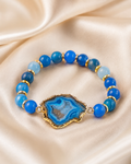 Blue agate bracelet with glossy blue beads and gold spacer accents displayed on ivory satin.