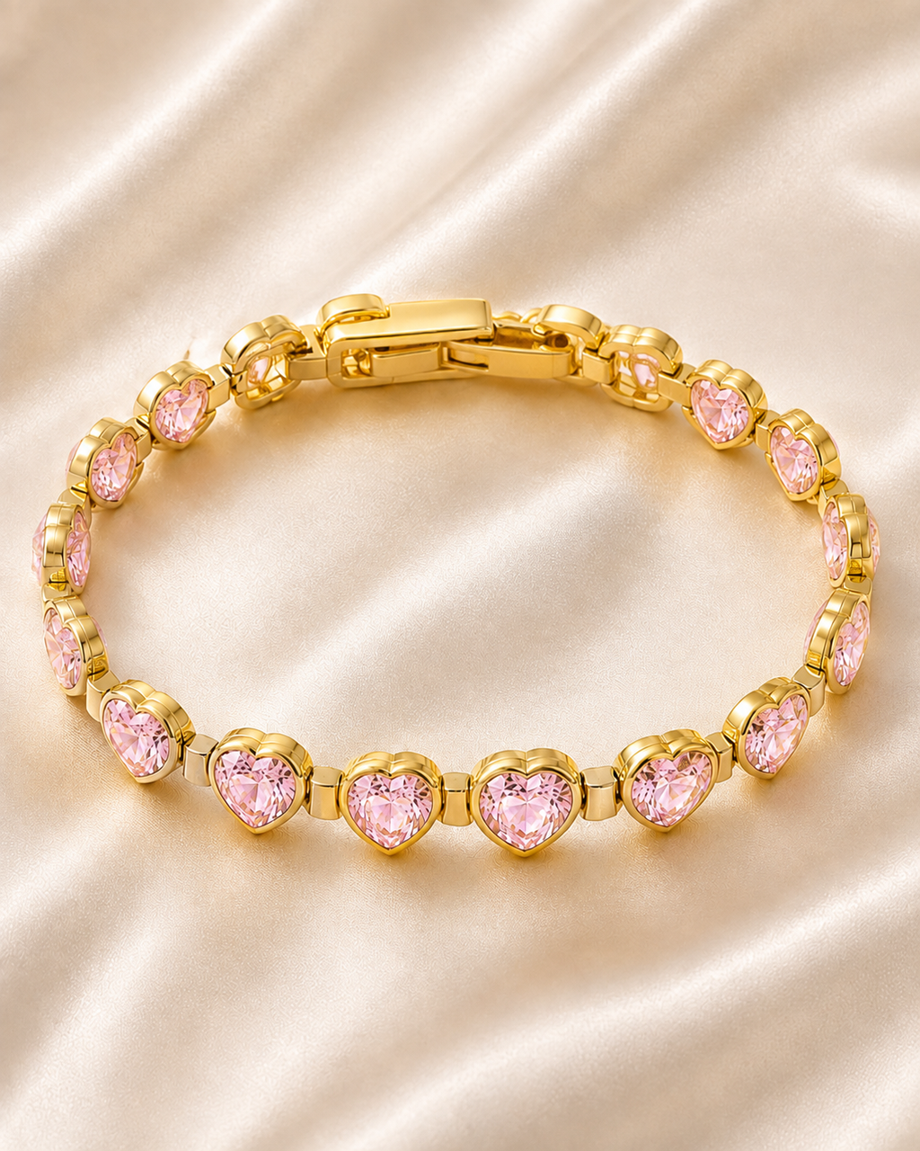 Pink Heartstone Bracelet with gold-tone links and sparkling pink heart-shaped stones displayed on soft satin fabric.