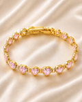 Pink Heartstone Bracelet with gold-tone links and sparkling pink heart-shaped stones displayed on soft satin fabric.