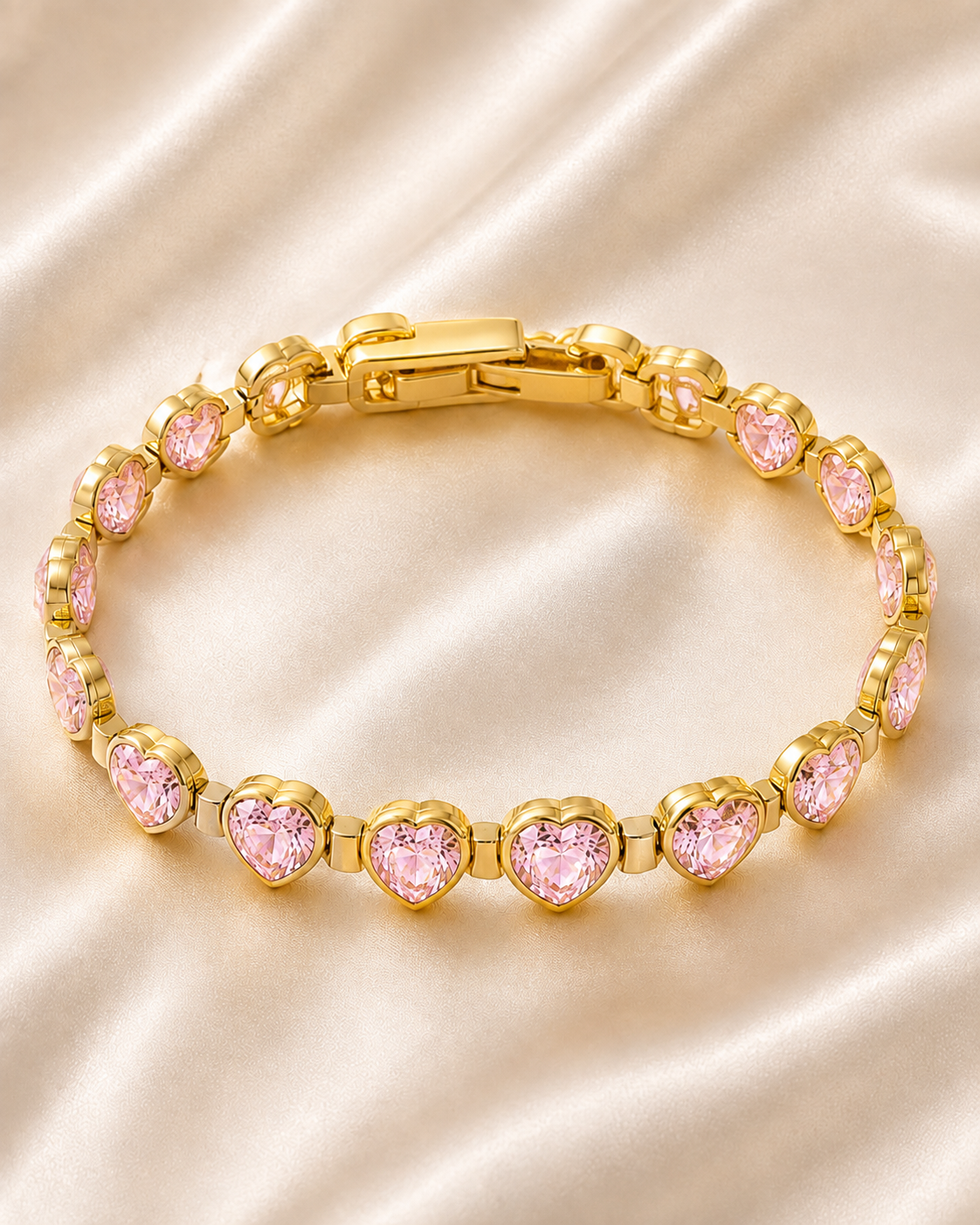 Pink Heartstone Bracelet with gold-tone links and sparkling pink heart-shaped stones displayed on soft satin fabric.