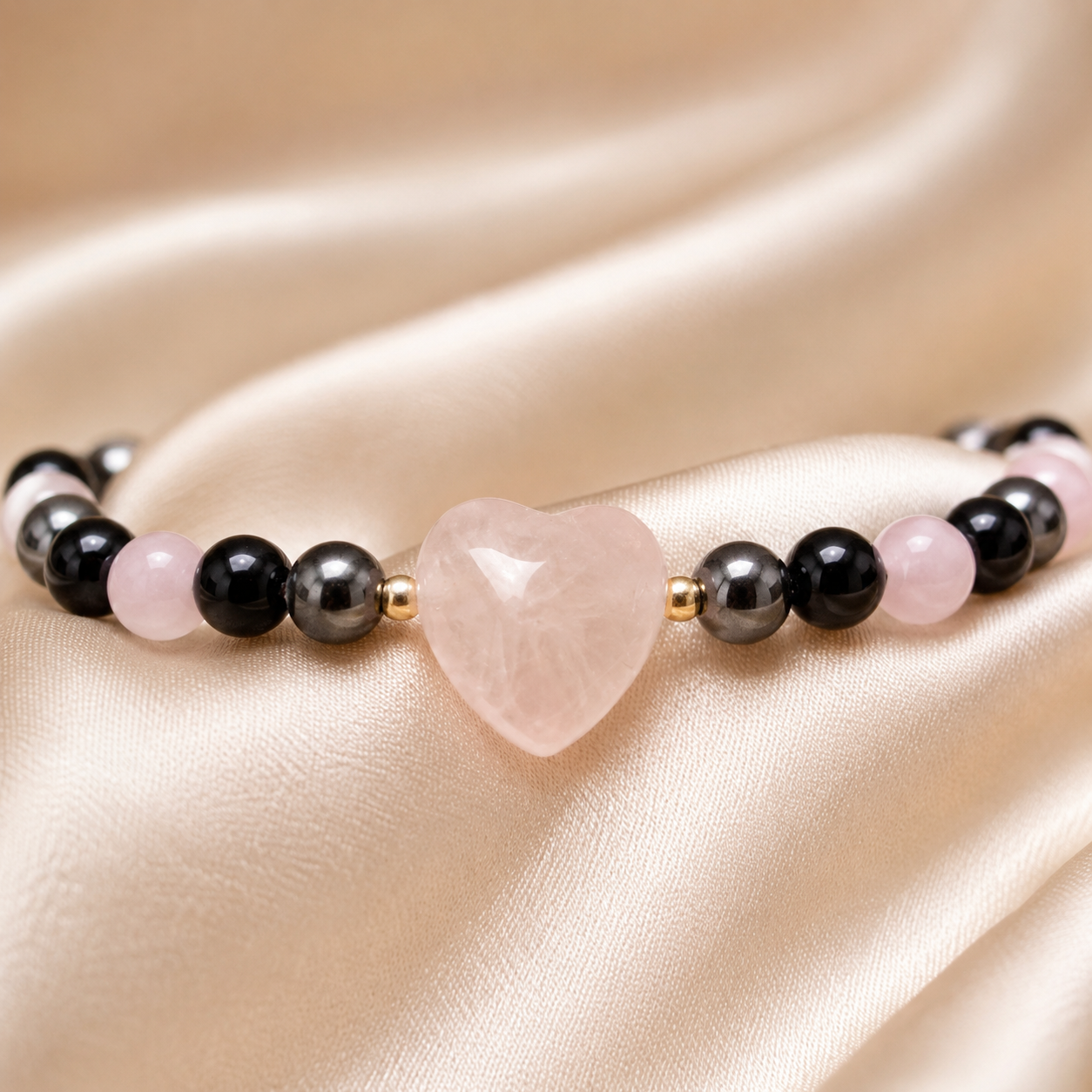 Close-up of pale pink heart centerpiece with black, metallic gray, soft pink, and gold accent beads.

