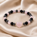 Rose Shadow Heart Bracelet with pink heart centerpiece, black beads, gray beads, soft pink beads, and gold accents on satin fabric.